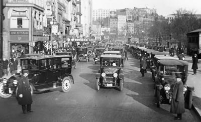 黑白照片描绘了一条挤满车辆的街道. 可以看到前景中有两个人在指挥交通.
