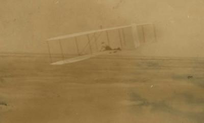 黄色的照片显示了一架有两个翅膀的滑翔机，一个人躺在中间，在飞行中