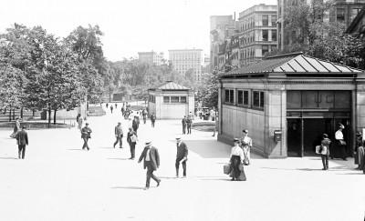 黑白照片描绘了一个地铁入口，许多穿着考究的男女走过. 照片中还有两个小男孩在向路过的人群卖报纸